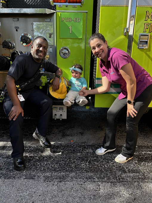 Children from a preschool participate in a Miami-Dade Fire Rescue Community Affairs visit, exploring a fire truck, viewing firefighting gear, and interacting with team members during a fire safety presentation.