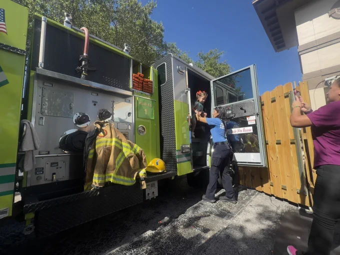 Children from a preschool participate in a Miami-Dade Fire Rescue Community Affairs visit, exploring a fire truck, viewing firefighting gear, and interacting with team members during a fire safety presentation.