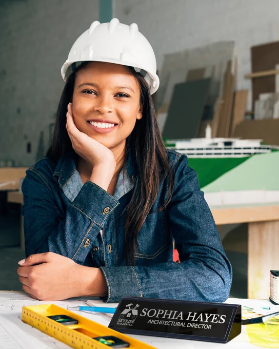 Happy Woman In White Hard Hat Leaning On Desk With Custom Black Piano Finish Desk Wedge Printed With Logo And Name And Role