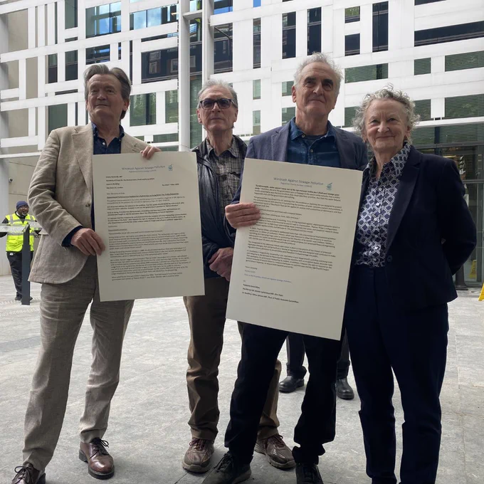 Four individuals stand outside a modern building holding large printed letters. The setting appears formal and serious.