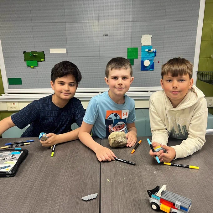 Three boys decorate rocks with colorful markers. 