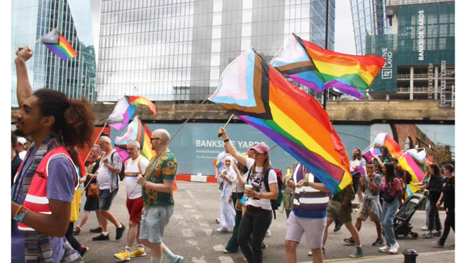 People marching in a Pride parade holding rainbow and transgender pride flags in Southwark.