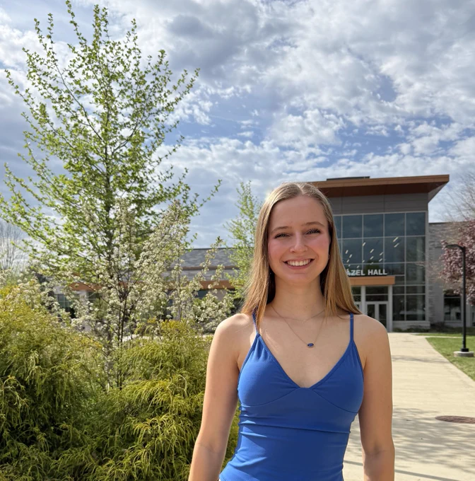 A young woman in a blue tank top smiles in front of an academic building and landscaping at the Fauquier Campus of Laurel Ridge Community Collee.