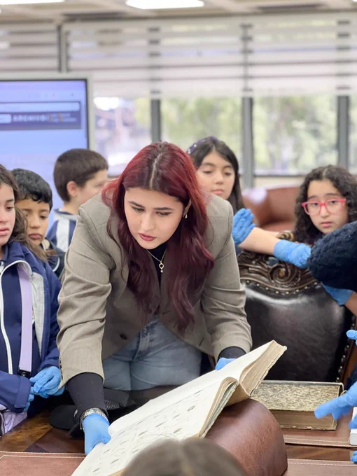 Integrante del equipo de Sala Chle muestra libro patrimonial a escolares durante visita a Biblioteca Central UdeC.