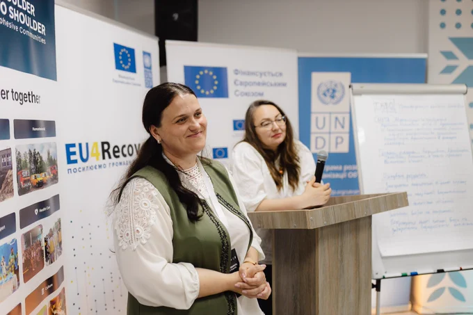 Two women facilitate a discussion during the interregional “Space of Unity – Shared Solutions” exchange visit. EU4Recovery, EU, and UNDP banners and flipcharts with participants’ notes are visible in the background as community representatives exchange ideas and experiences.
