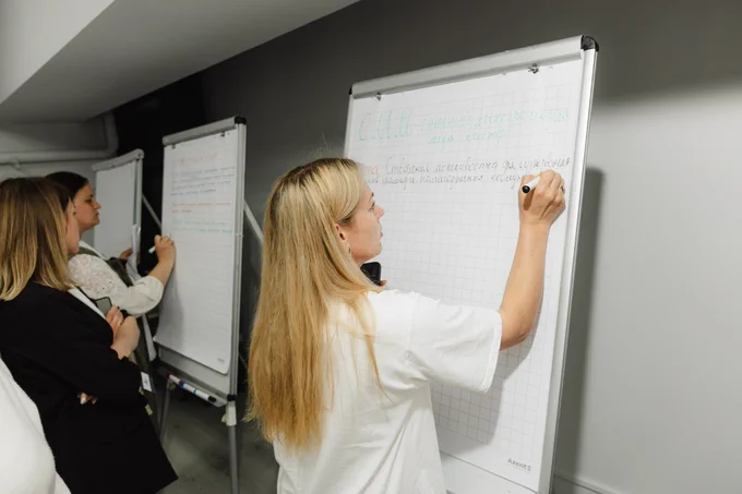 Participants (three women) write ideas on flipcharts during a group exercise at the interregional “Space of Unity – Shared Solutions” exchange visit, contributing to discussions on community recovery and cooperation.