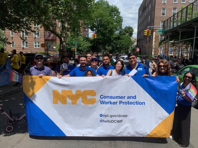 A group of people march in the Queens’ Pride Parade, holding a banner that reads: N Y C Department of Consumer and Worker Protection.