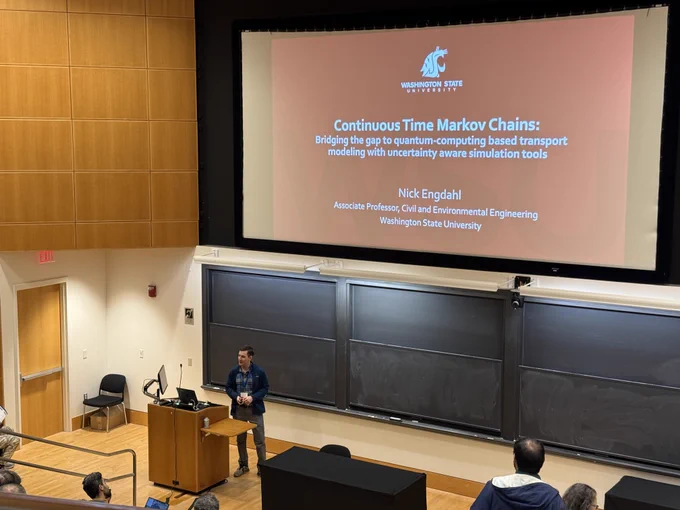 Nick Engdahl presents his featured talk, "Bridging the Gap to Quantum Computing-Based Hydrological Modeling with Uncertainty-Aware Simulation Tools," with his title slide displayed behind him.