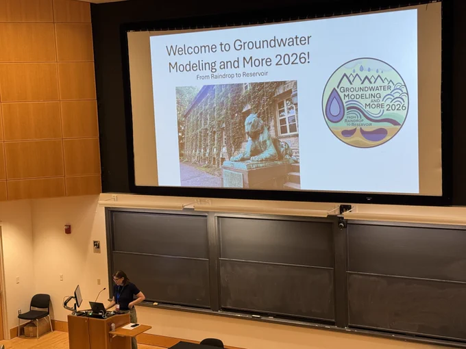 Laura Condon welcomes attendees to Day 2 of Groundwater Modeling and More 2026, with the conference logo displayed on a title slide behind her.