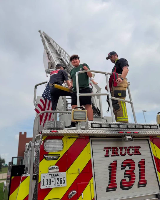 Firefighters on a fire truck with emergency lights, American flag, and text "TRUCK 131" visible.