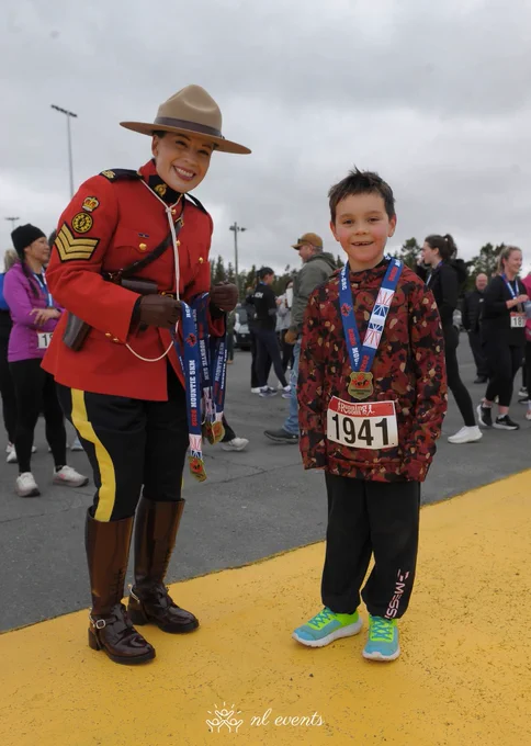 A RCMP officer dressed in red serge stands next to a smiling child wearing a medal.