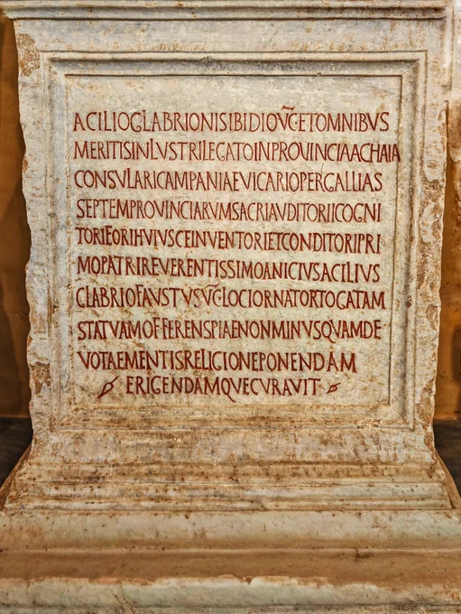 DEDICATION ON STATUE BASE, 438 CE. VATICAN MUSEUMS

​Here we find a large white marble statue base with an inscription that notably has its rubrication, the red paint in the incised letters, intact or restored, making the text leap out at the reader. This C5 honorific text dedicates a togate statue to the high-ranking official Acilius Glabrio Sibidius from his powerful son, Anicius Acilius Glabrio Faustus, the ordinary consul for the year 438. The text lists the father's career, including serving as Vicar of the Seven Provinces of Gaul and founder of the local forum. The letterforms mimic the elegant, serif-heavy Filocalian or Damasian style of the late C4, but the execution betrays a distinct technical decline in monumental craftsmanship, where lines visibly droop downward to the right, vertical stems wobble, and poor layout planning forces the word ACHAIA to clumsily breach the right-hand frame.