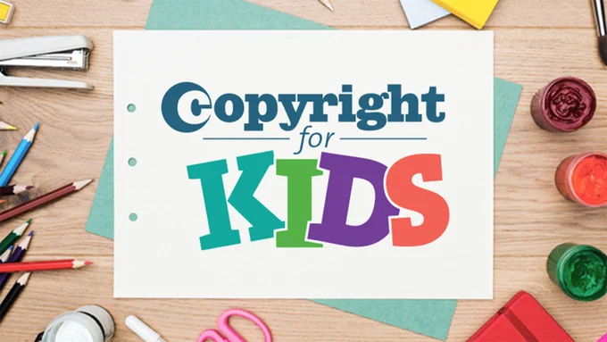 White sheet of paper with three hole-punched holes reads, "Copyright for Kids." The sheet of paper sits on top of a wooden table and is surrounded by various art supplies. 