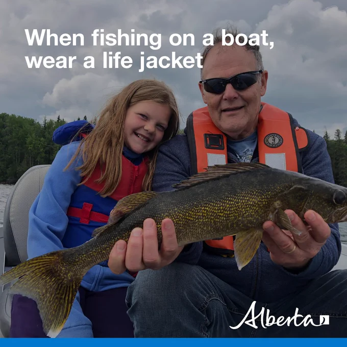 image depicts a man and child donned in life jackets posing with a caught fish. Text reads When fishing on a boat, wear a life jacket with the white Alberta logo in the bottom right corner.