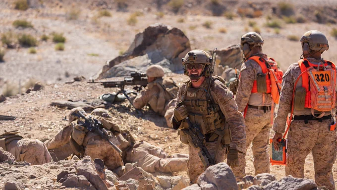 A Marine communicates while maneuver elements and machine gun teams conduct live-fire operations on a desert range.