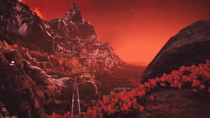Dramatic red-tinted mountain landscape in Once Human, with snow-covered peaks under a fiery red sky, vibrant red flowers in the foreground and a long bridge winding through the valley.