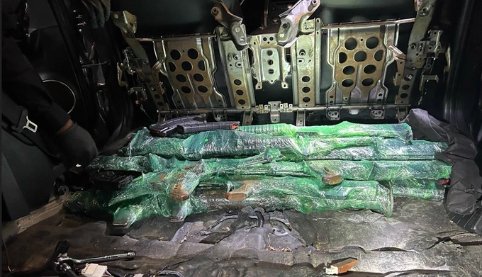 Several long weapons wrapped in green plastic and tape are laid out inside a vehicle with exposed metal panels.