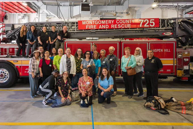 Group of diverse adults posing in front of Montgomery County Fire and Rescue truck inside fire station.