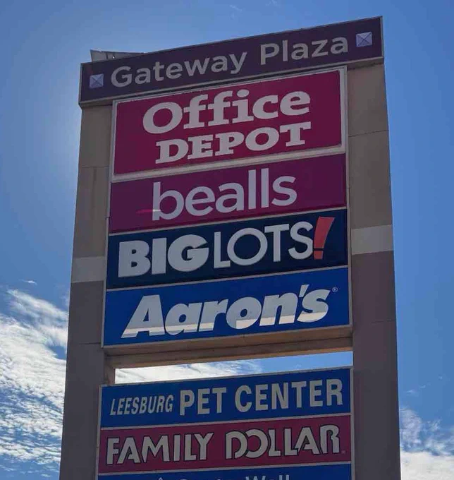 A large sign displaying various store names located at Gateway Plaza under a sunny sky. The mood is commercial and business-oriented.