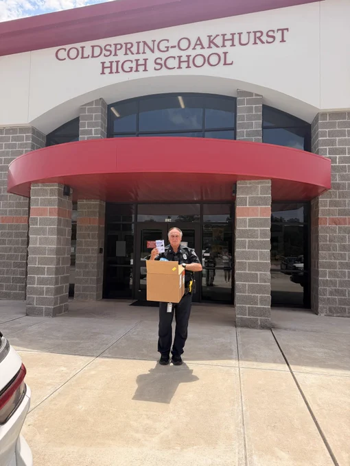 Coldspring-Oakhurst High School police officer outside the Coldspring, Texas campus holding a large box of Padagis naloxone and a single box, showing Carry Hope Naloxone’s overdose prevention work in schools.