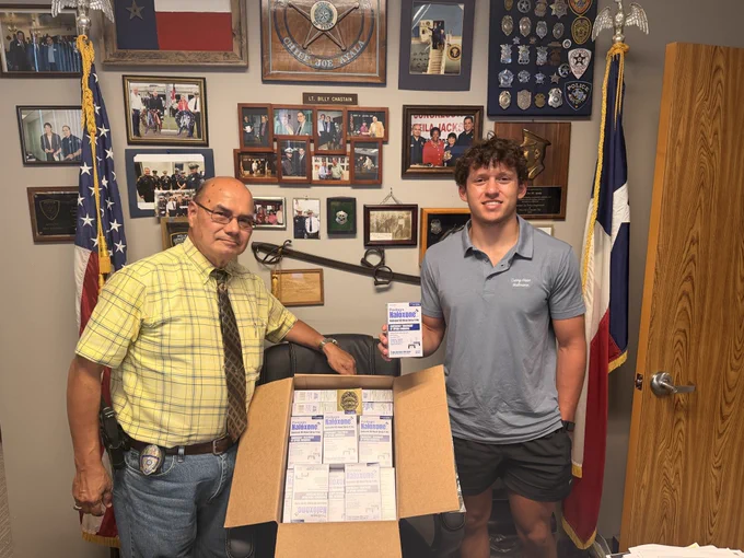 Jacinto City Police Chief and Carry Hope Naloxone founder Peyton Eitel in the Jacinto City, Texas police chief’s office with a large box of 100 Padagis naloxone units and a single box, emphasizing new naloxone access for officers.