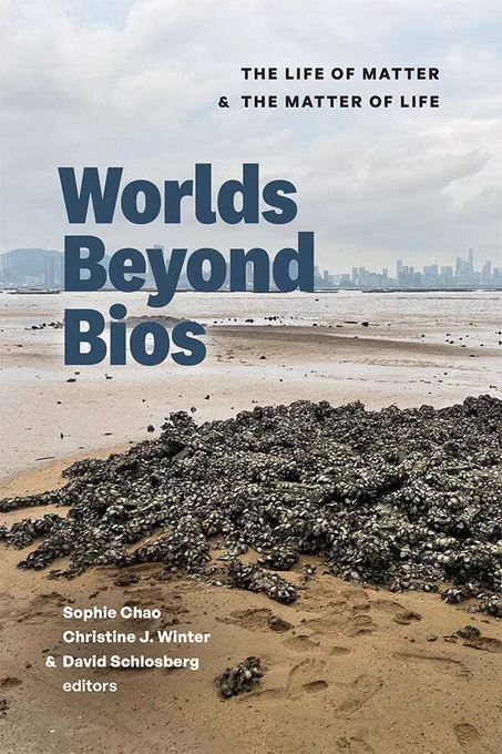 Cover of Worlds Beyond Bios: The Life of Matter and the Matter of Life edited by Sophie Chao, Christine J. Winter, and David Schlosberg. The cover features a photograph of a sandy beach with a city skyline stretched out in the distance. The foreground shows wet sand, footprints, and a large pile of organic material. The title is written in a bold sans serif font in grey blue aligned left. The subtitle is written in black and all caps above and aligned right. The editors names are in white in the bottom left. 