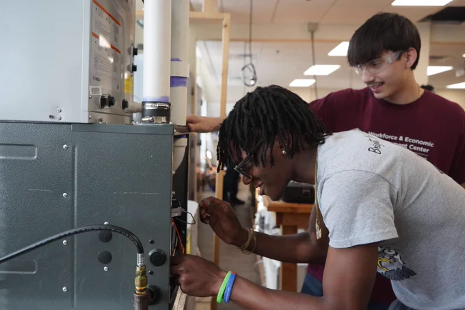 Two students working on an HVAC unit in a classroom setting.