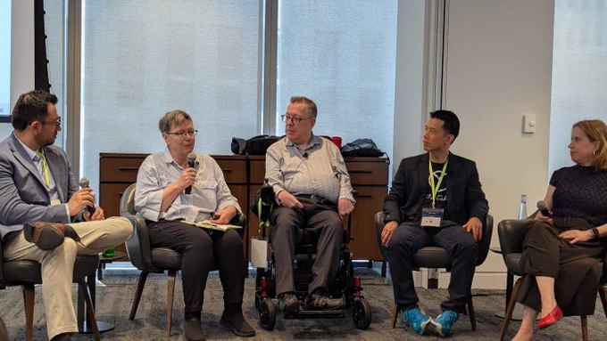  AI and Accessibility panel discussion at the A11yVerse x IAAP Canada Summit featuring representatives from A11YVERSE / Digita11y Accessible, Microsoft, Salesforce, OCAD University, and Venngage. Five speakers are seated at the front of a conference room, discussing how artificial intelligence can support accessibility and inclusive technology development. One panelist uses a power wheelchair. Large windows behind the speakers provide natural light throughout the room. 