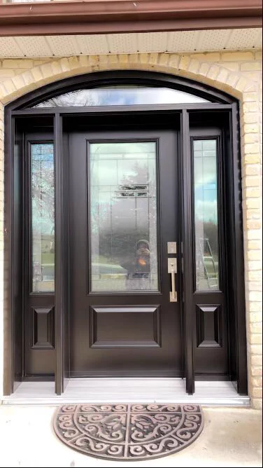 Custom-painted black entry door with decorative glass sidelights and elliptical transom window installed in brick home entrance.