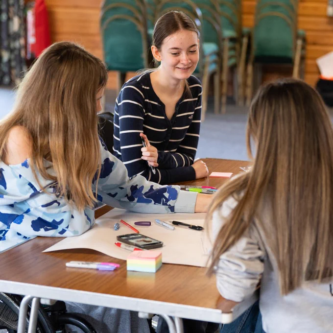 Photo of three young people engaged in a collaborative discussion and writing task during a Back Up Youth Advisory Group weekend.