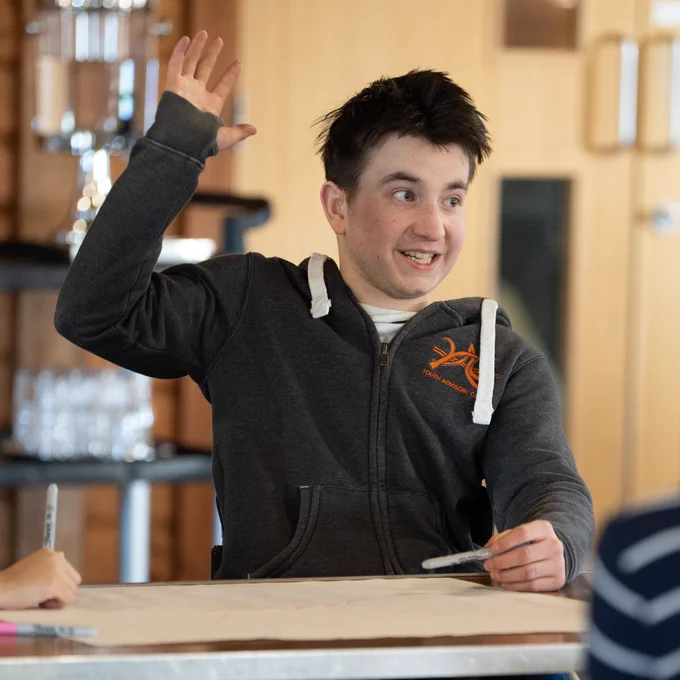 Photo of a young person raising their hand during a group activity on a Back Up Youth Advisory Group weekend.