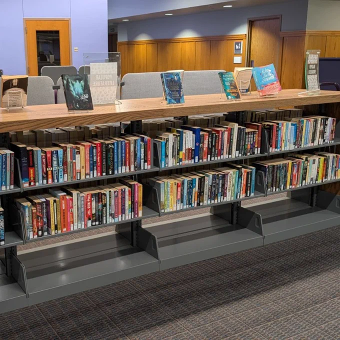 A wooden book shelf with books displayed on the top, and books in the shelves.