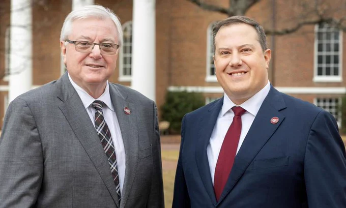 University of South Carolina President Michael Amiridis and Board of Trustees Chair That Westbrook pose in front of a beautiful brick building with columns on the University of South Carolina Horseshoe.