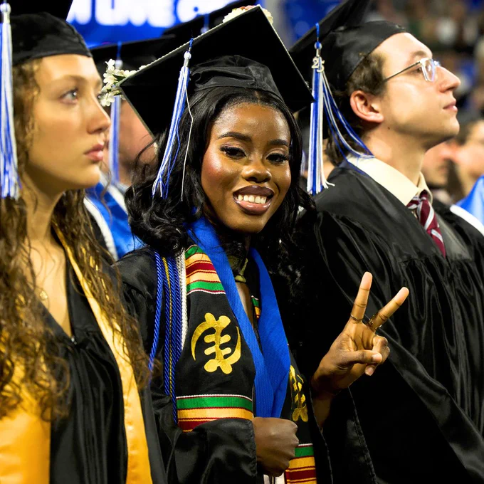 Student flashing a peace sign smiling in graduation cap and gown