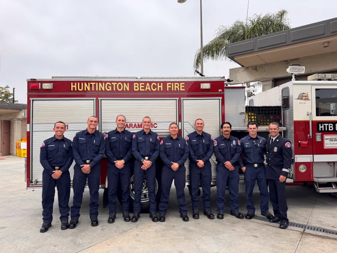 The six graduates of the Huntington Beach Fire Department's 2026 Firefighter Paramedic Academy pose with academy instructors and department leadership in front of a Huntington Beach fire engine following their graduation ceremony. The group stands proudly in Class B uniforms as the newly graduated firefighter paramedics prepare to begin their one year probationary assignments on engine companies throughout the city.