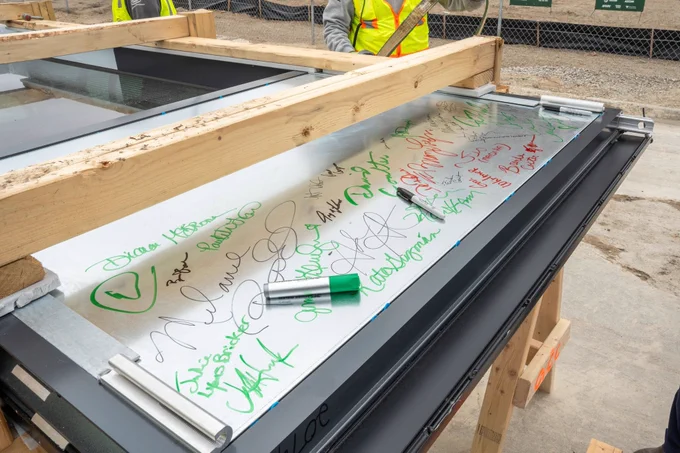 Close-up of a metal panel covered with handwritten signatures and markers at a construction site.