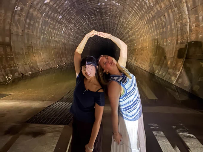 Two people stand side by side inside a large, lit tunnel