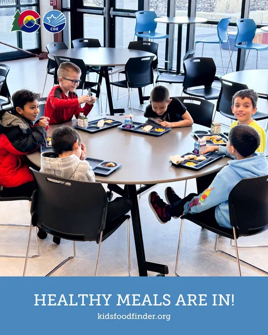 A group of six young children sit around a cafeteria table, enjoying meals on trays. The room has large windows letting in natural light. At the top left, logos for Colorado Proud and CDE (Colorado Department of Education) are visible. A message at the bottom reads, "Healthy meals are in! kidsfoodfinder.org".