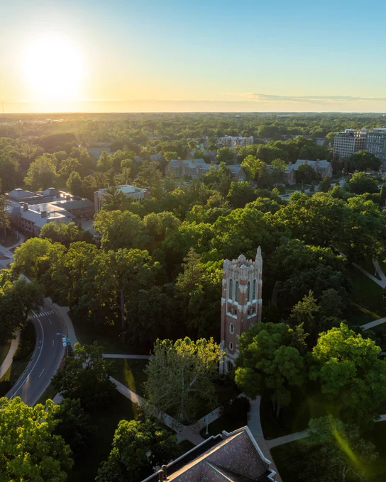 Aerial view of Beaumont Tower rising above trees on Michigan State University\u2019s campus at sunset.