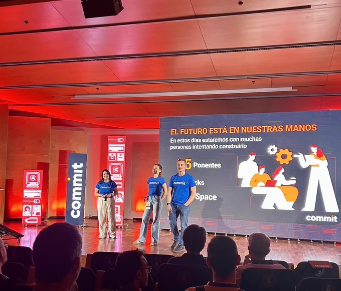 Isa Rodríguez, Laura Vignali y Abraham Otero presentan Commit Conf desde el escenario principal del evento. Frente a una audiencia llena de asistentes, comparten la bienvenida mientras detrás de ellos se proyecta una gran pantalla con información sobre la conferencia y el mensaje "El futuro está en nuestras manos". La imagen refleja el inicio de una jornada centrada en la comunidad, el aprendizaje y el intercambio de conocimiento.