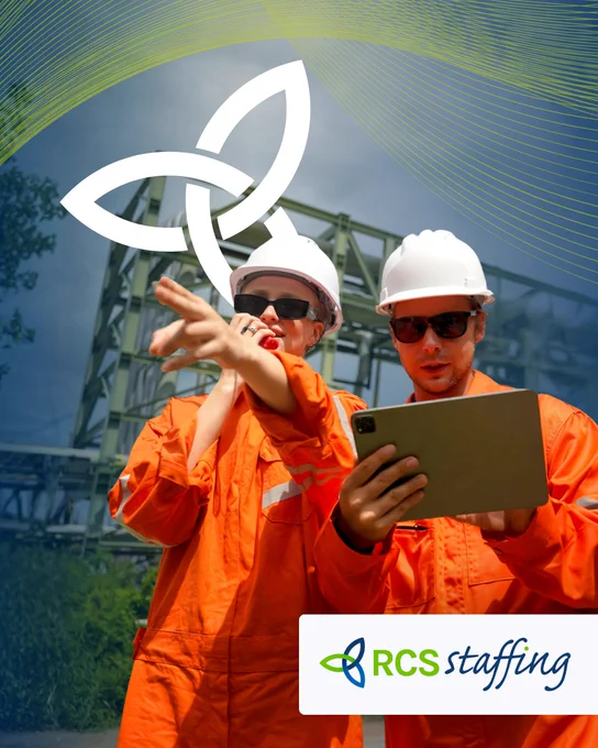 Two workers in orange uniforms and hard hats discuss plans at an industrial site. The mood is professional and collaborative.