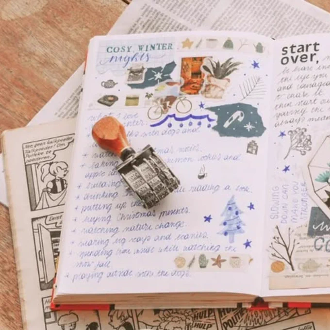 Open journal spread with winter-themed illustrations, handwritten notes, and decorative stickers on a wooden table.