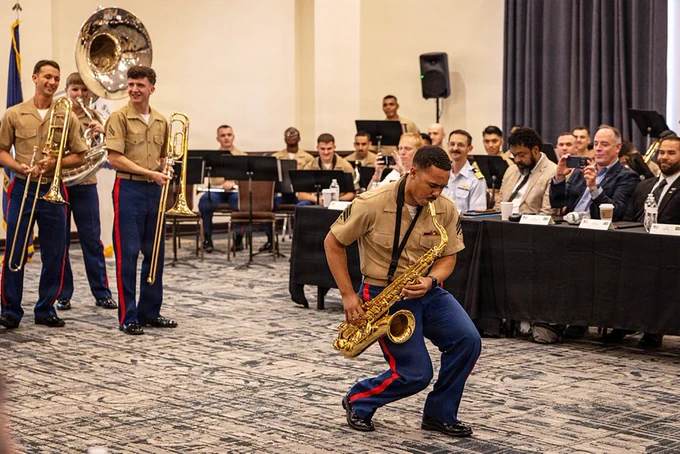 A Marine Forces Reserve Band saxophonist performs during a musical demonstration as military leaders and guests observe from conference tables.