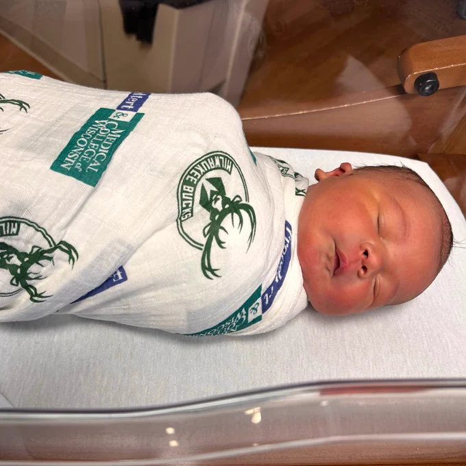 A photo of a newborn baby wrapped in a Froedtert and MCW Bucks blanket.