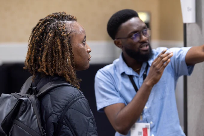 A male scientist talks about his research with a female scientist during a poster session at a scientific research conference.