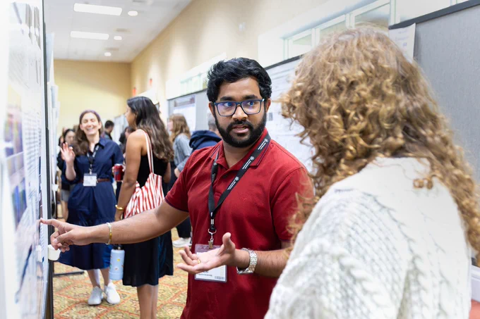 A male scientist talks about his research with a female scientist during a poster session at a scientific research conference.
