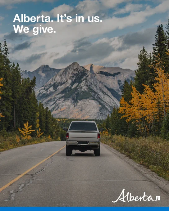 Photo of back of a pick up truck as it drives towards mountains. Text reads: “Alberta. It’s in us. We give.” Alberta logo is in bottom right corner. 