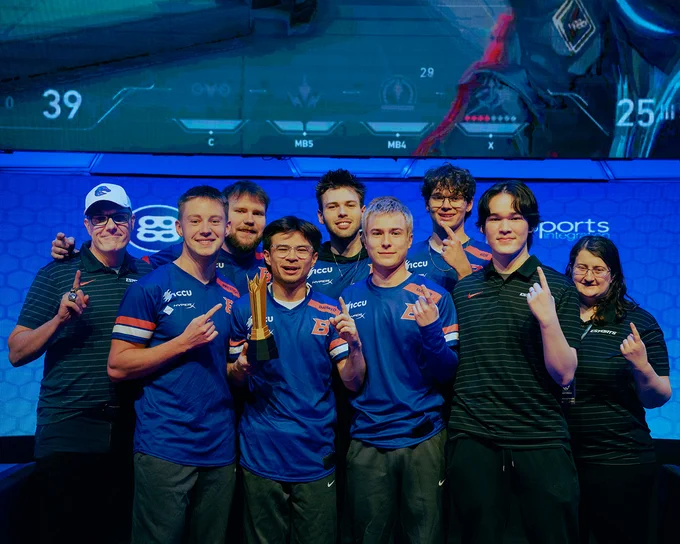 Kelsey Moser, a Boise State economics graduate student and the associate coach for Bronco Esports pointing up and smiling with her players and other esports coach.
