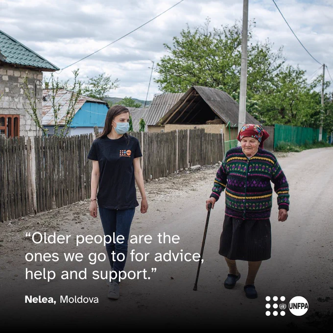 A photo of a young woman in a UNFPA shirt walking alongside an older woman in a colourful jumper, using a walking stick, on a village road. The setting includes a wooden fence and houses. A quote from Nelea, from Moldova, in white text overlaid reads: "Older people are the ones we go to for advice, help and support." The UNFPA logo is in the bottom right corner.