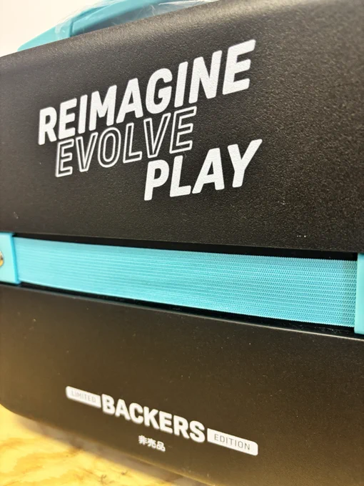Close-up of a box with motivational phrases 'Reimagine, Evolve, Play' printed on it. Labeled 'Limited Backers Edition.'